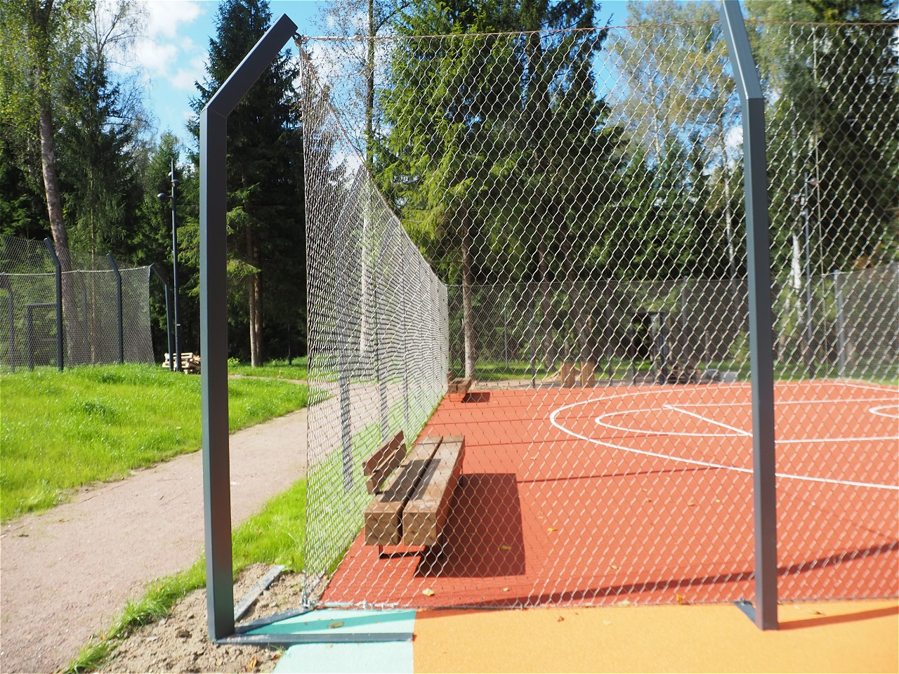 Side profile view stainless steel rope fence around forest park basketball court with wooden bench inside
