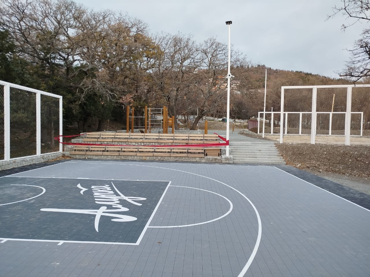 Panoramic full site shot of dual sports field mesh enclosure on wooded hillside